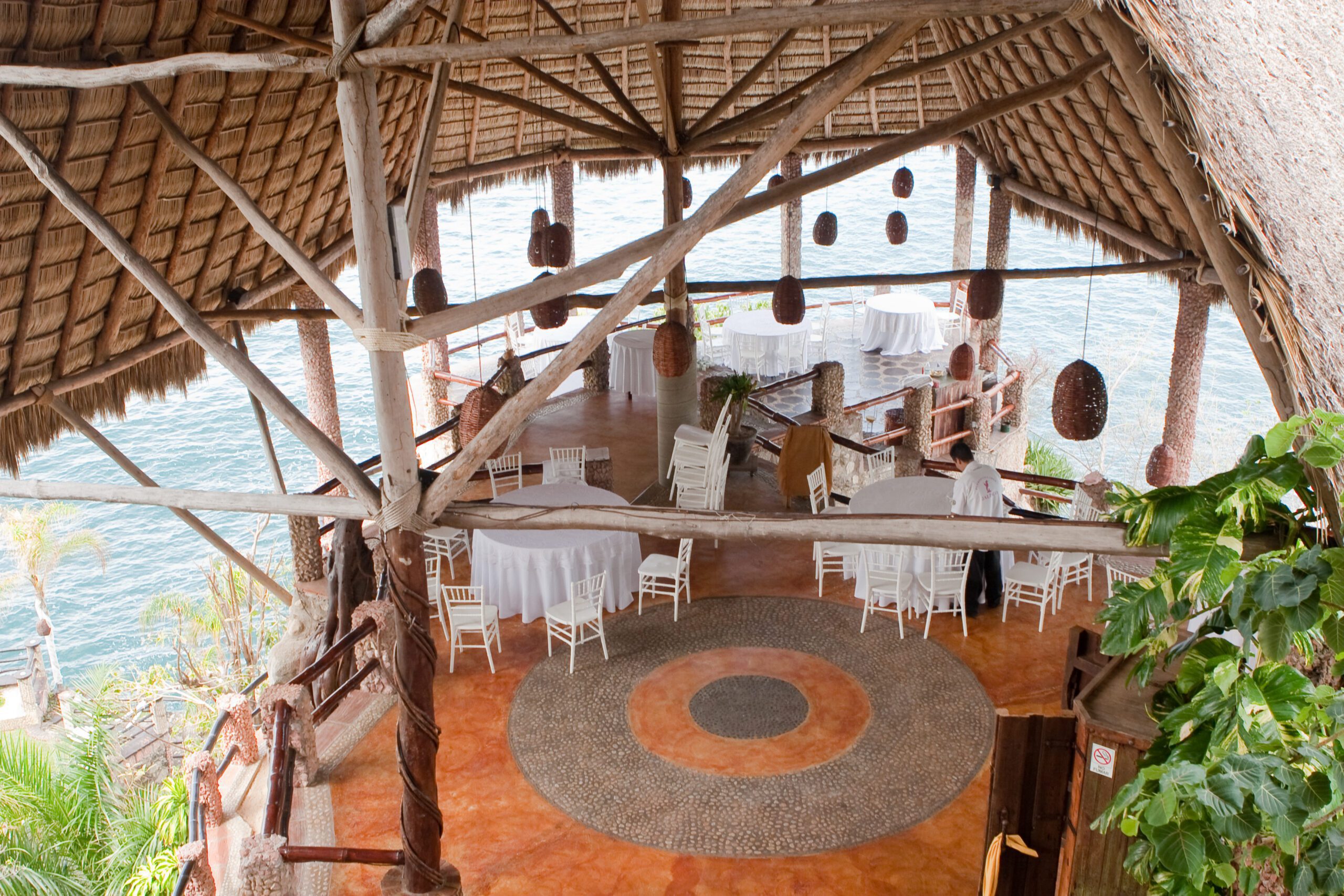 This is a picture of the inside of the Le Kliff from 2010. Unfortunately, a hurricane took the structure down. It is showing the lowest two level with round tables, white table cloths, and white chairs. The it is a thatch roof with wooden beams holding it up. It is surrounded by the ocean on three sides.
