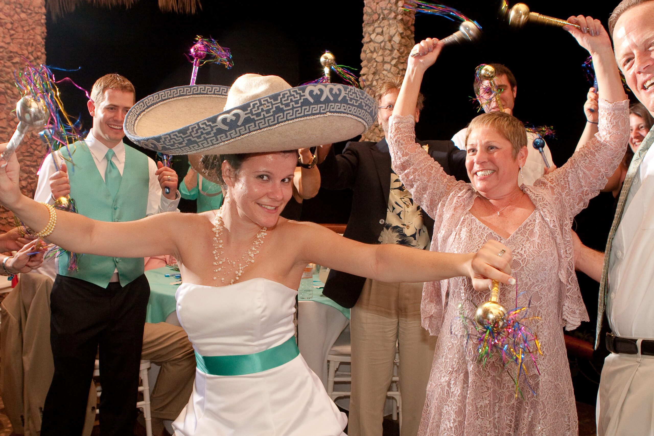 This is a photo primarily of Anna dancing with a Marachi hat on top. One of the dinner guest had taken the Marachi's hats and put it on top of Anna's head. They were extremely upset, but she looks super cute wearing it. In her hands, she has maracas that she's shaking. Surrounding her is all the friends and family also shaking their maracas.