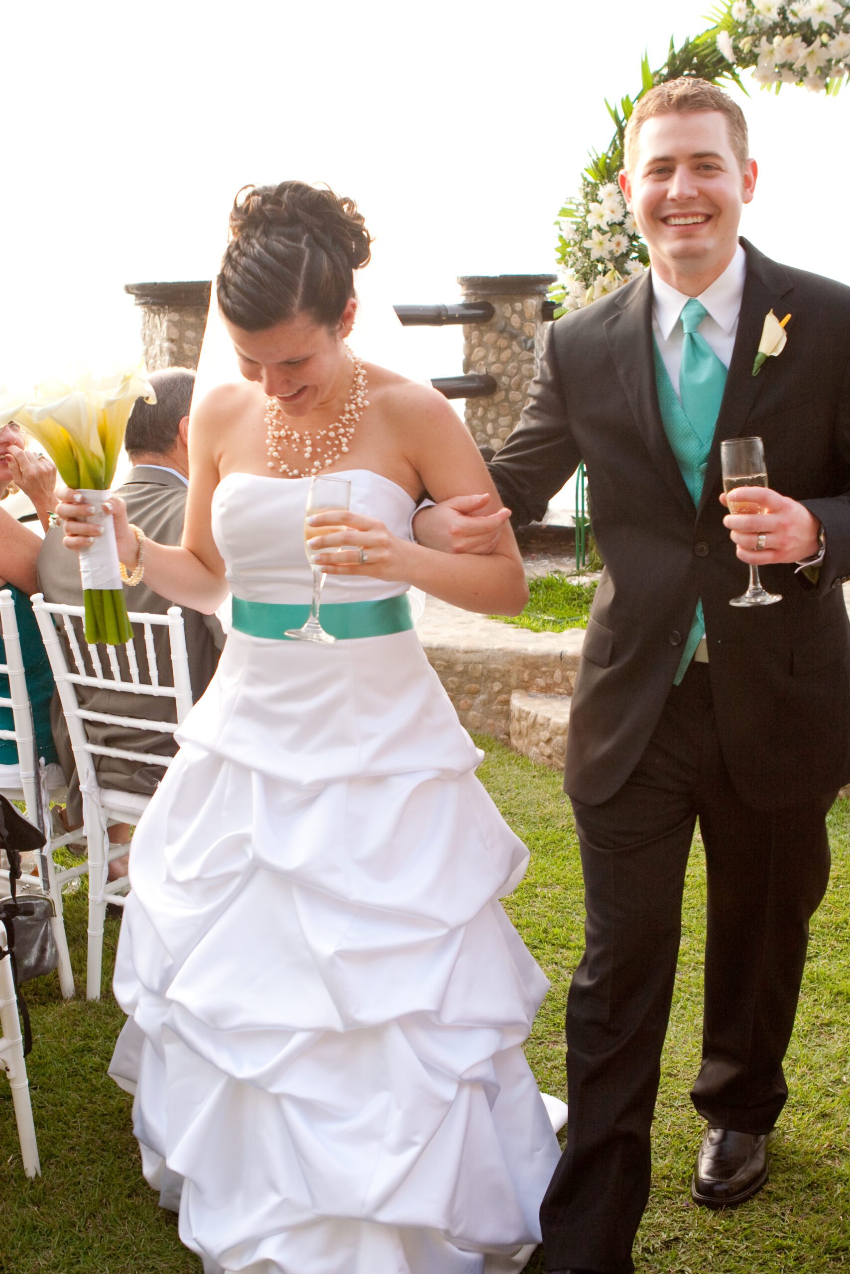 Vertical photo of Adam and Anna walking away from the wedding venue holding a glass of Champagne.