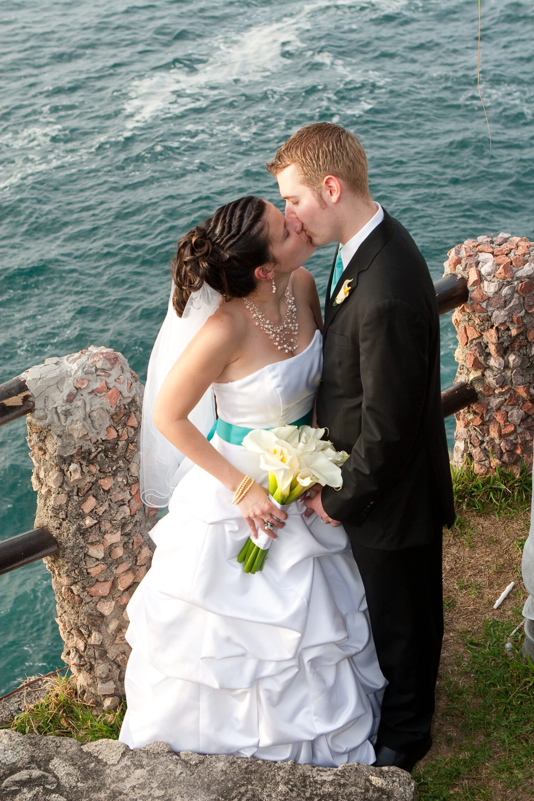 Anna and Adam, kissing with the ocean in the background on the edge of the restaurant. It is a vertical top down photo.